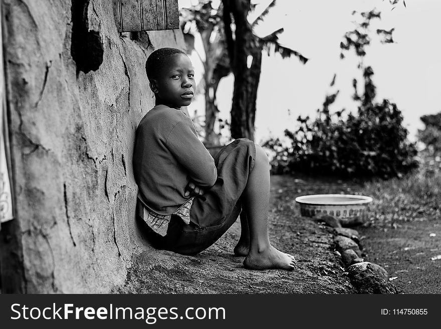 Greyscale Photography of Boy Sitting Behind Wall