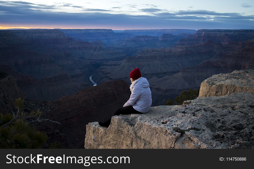 Person Wearing White Hoodie Sitting on Cliff at Daytime