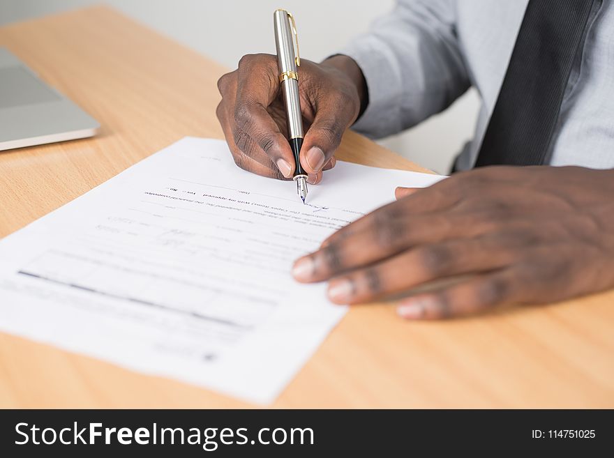 Person Holding Gray Twist Pen and White Printer Paper on Brown Wooden Table