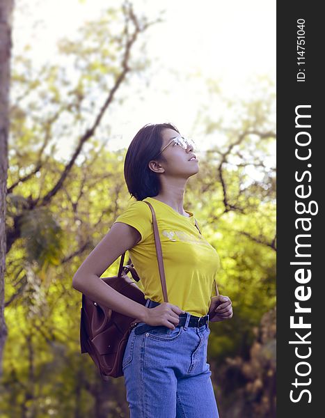 Woman Wearing Yellow Shirt and Looking Up Surrounded by Trees