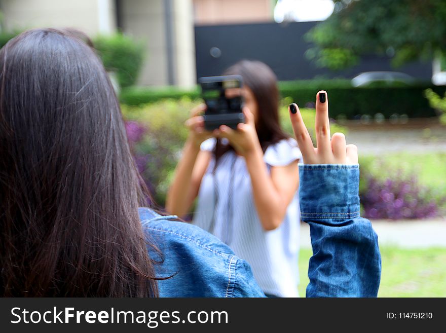 Woman Holding Camera While Taking Picture Of A Woman With A Peace Finger Sign