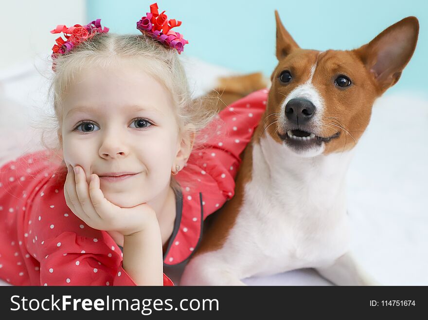 Little blonde curly girl hugging a red basenji dog.