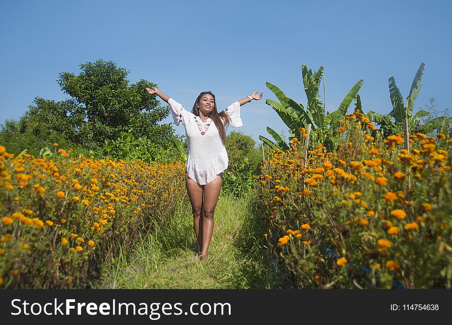 Happy and beautiful young Asian woman relaxing enjoying the fresh beauty of gorgeous orange marigold flowers field natural landscape in travel destination and holidays Summer trip tourist excursion
