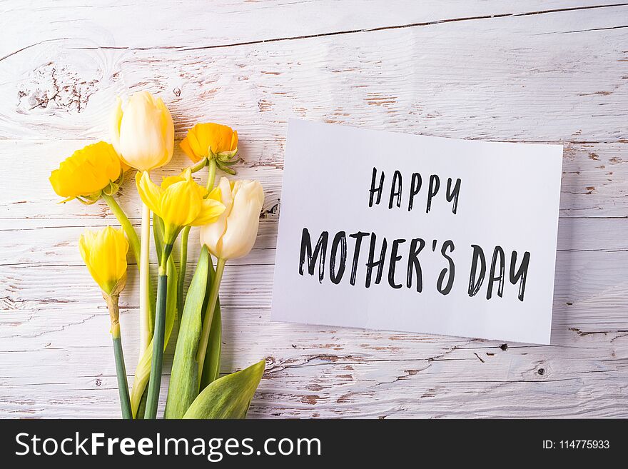 Mothers day composition. Happy mothers day note and bouquet of yellow flowers. Studio shot on white wooden background. Flat lay. Mothers day composition. Happy mothers day note and bouquet of yellow flowers. Studio shot on white wooden background. Flat lay.