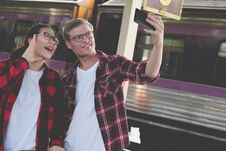 Man & Woman Use Smart Phone To Take Selfie Photo At Train Station. Traveler Couple Travel Together On Holiday Royalty Free Stock Image