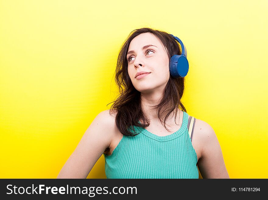 Young woman with eyes up listening to music on yellow background in studio