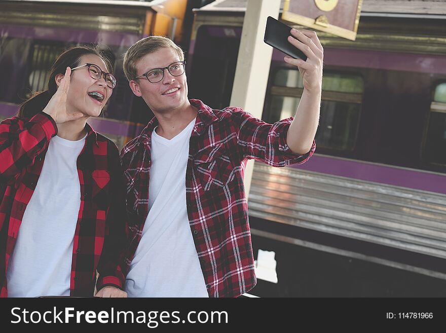 caucasian men & asian women use smart phone to take selfie photo at train station. traveler couple travel together on holiday. caucasian men & asian women use smart phone to take selfie photo at train station. traveler couple travel together on holiday