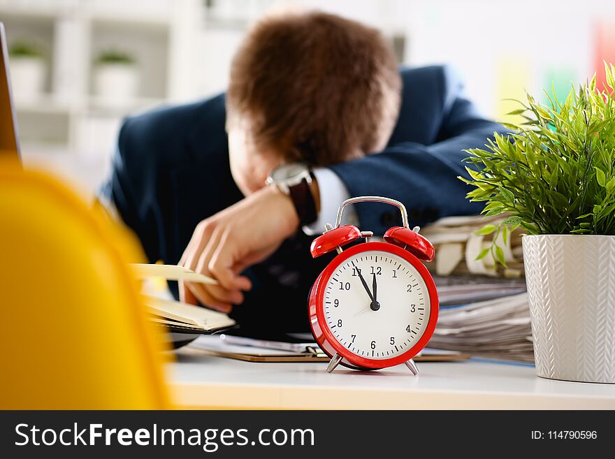 Red alarm clock shows late time closeup and tired office male clerk in suit take nap on table workplace full of exam papers. Career frustration freelance employment fail study problem low energy down