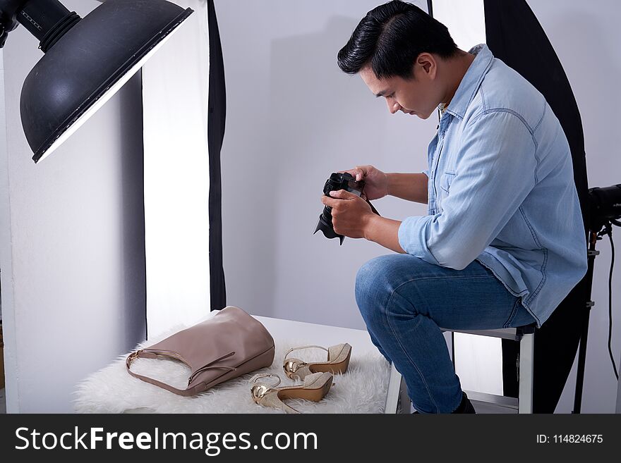 Young Vietnamese man taking photos of fashion items in studio. Young Vietnamese man taking photos of fashion items in studio