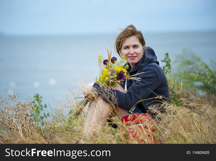Woman Sitting on Grass Holding Flowers Wearing Black Hoodie