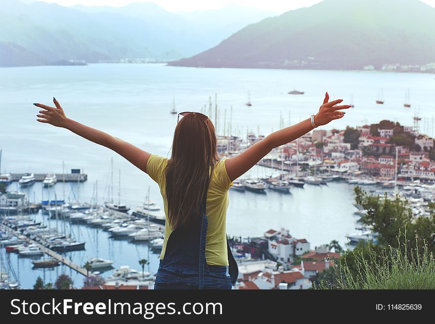 Woman Raising Her Hands Facing Cityscape Near Body of Water