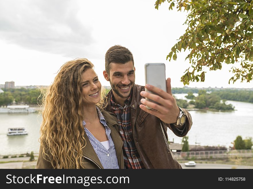 Man Holding Smartphone Beside Woman Near Tree