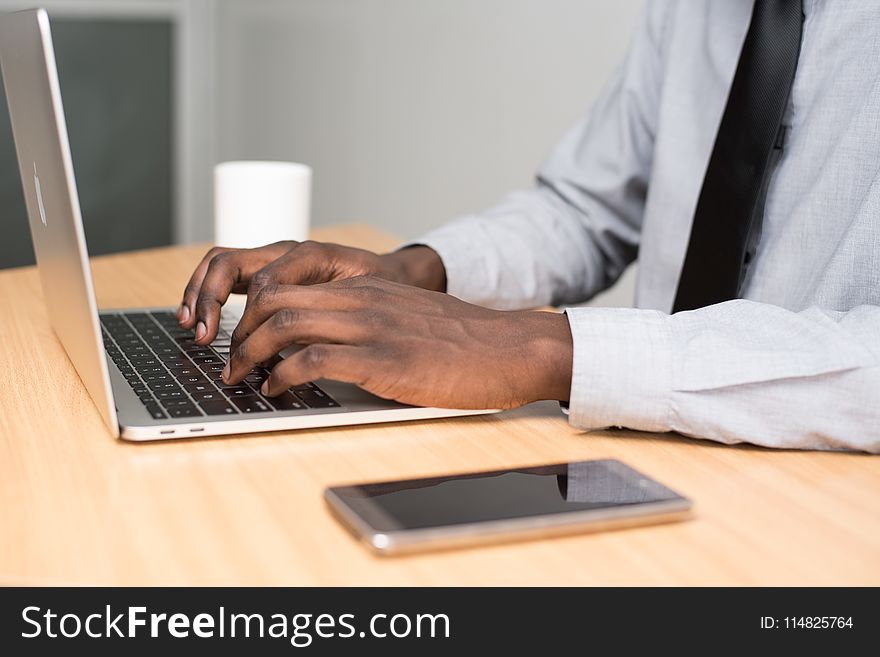 Person Wearing White Dress Shirt and Black Necktie Using Macbook Air on Beige Wooden Table