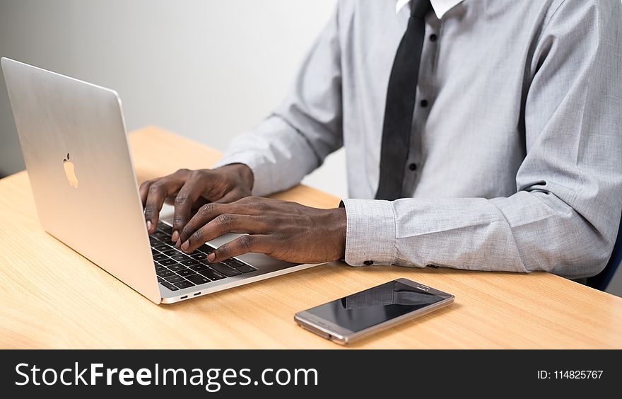 Person Sitting In Front Of Table Using Laptop Beside Smartphone