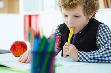 Curly Caucasian Boy Thought About The Task And Took A Pen In His Mouth During The Lesson At School. Education, Childhood Royalty Free Stock Image