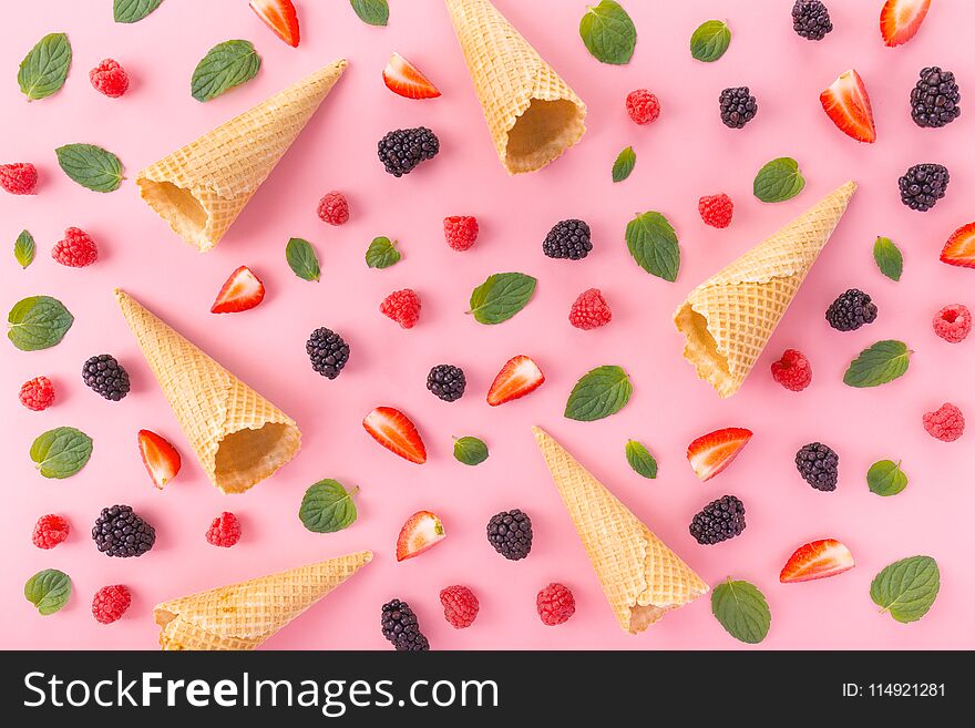 From above view of empty waffle cones in arrangement with mixed berries and mint leaves on pink. From above view of empty waffle cones in arrangement with mixed berries and mint leaves on pink.