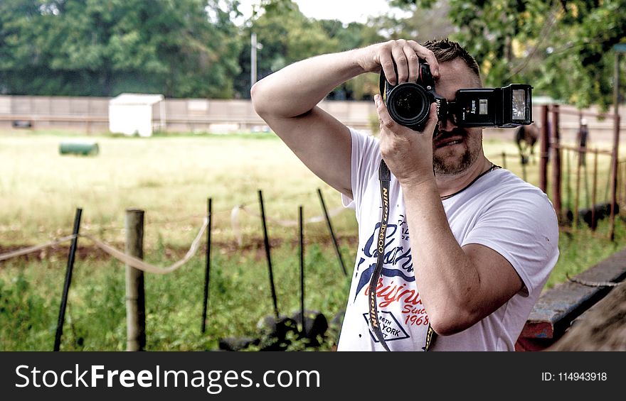 Man Holding Dslr Camera While Standing Near Fence