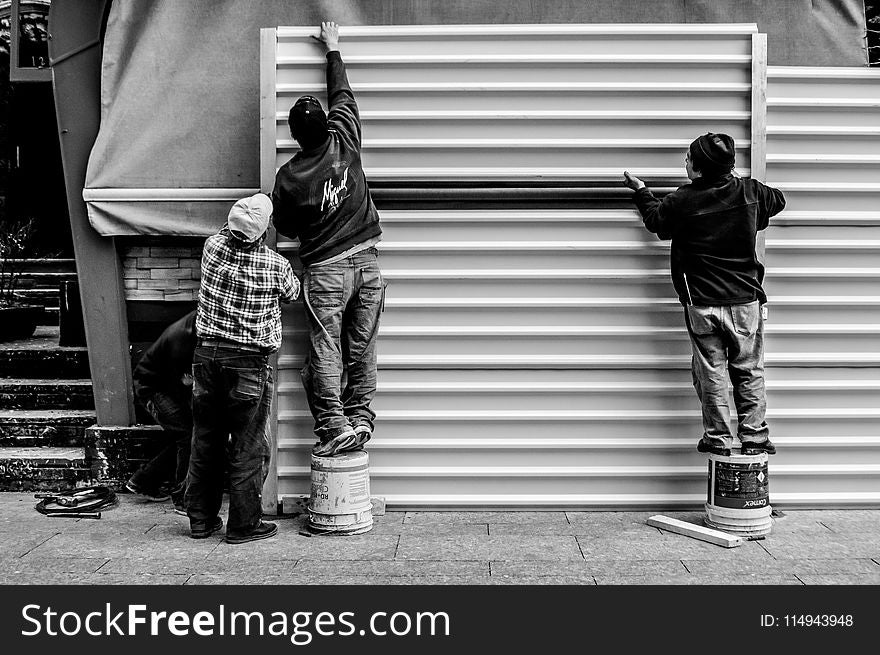 Grayscale Photo Of Three Men Arranging Metal Wall