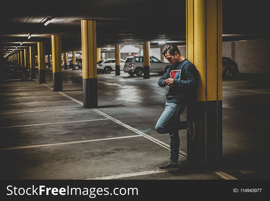 Man In Dark-gray Crew-neck Sweater Standing Leaning To Post In Parking Lot