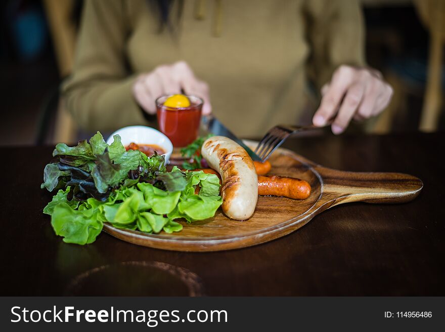 Woman holding knife and fork for eating food, close up Sausage with Tomato Sauce and green vegetable on wood plate