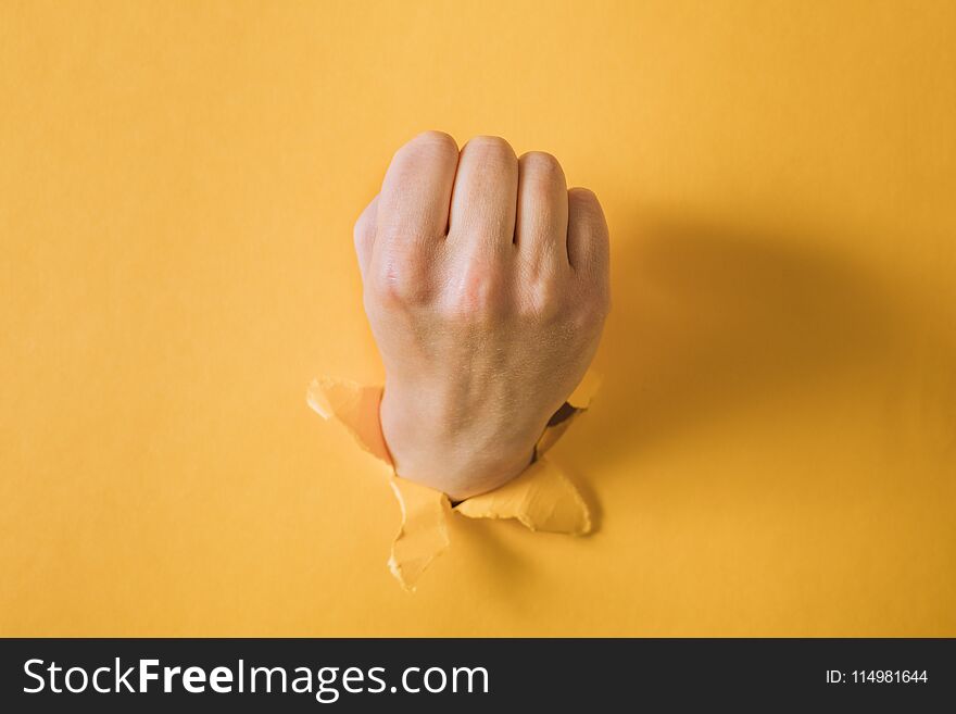 Female Fist Punching Through A Paper, Isolated On A Yellow Background.