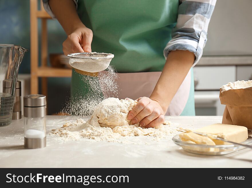 Woman sprinkling flour over dough on table in kitchen