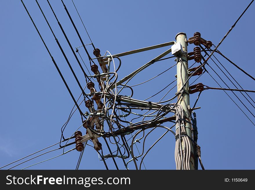 A jumble of telephone cables and a telegraph pole against a clear blue sky.