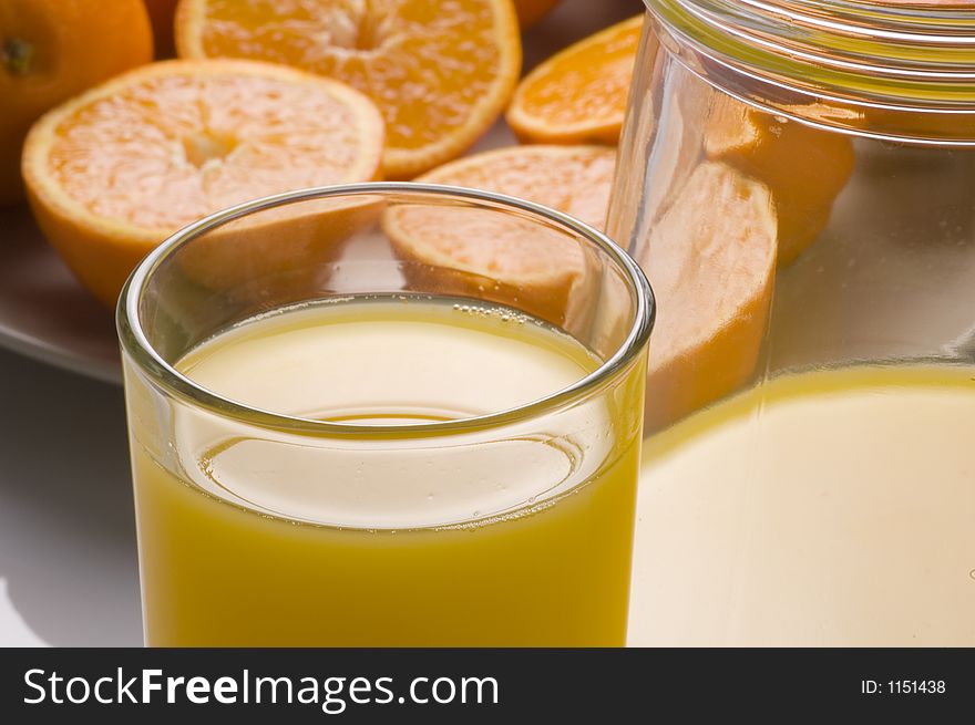 A glass and jug of orange juice with a background of fresh oranges