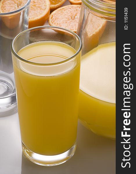 A glass and jug of orange juice with a background of fresh oranges