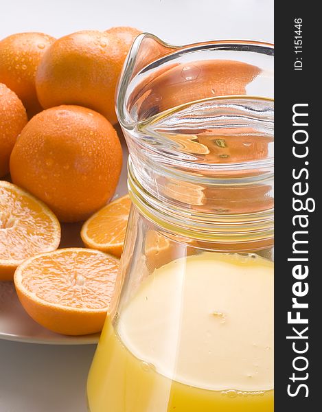 A glass and jug of orange juice with a background of fresh oranges