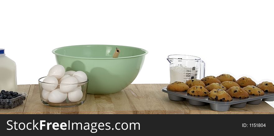 Table with blueberry muffins, mixing bowl, ingredients.