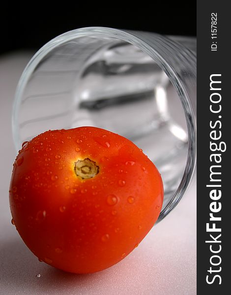 A fresh, red tomato which is infront of a glass. A fresh, red tomato which is infront of a glass.