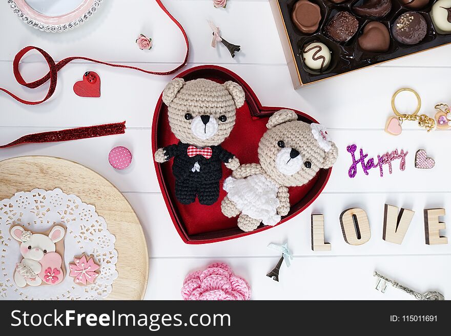 Happy anniversary present : bride and groom teddy bear crochet dolls or amigurumi, handmade bunny cookies and a box of chocolate on the white wooden board. Romantic Valentines gift. Selective focus.