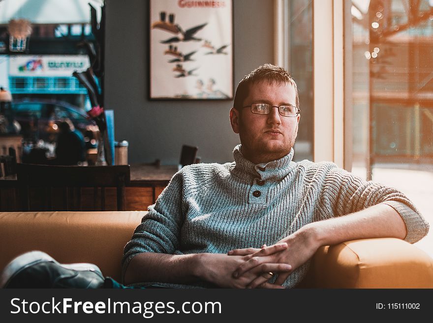 Man Wearing Gray Knitted Sweater Sitting on Brown Fabric Sofa