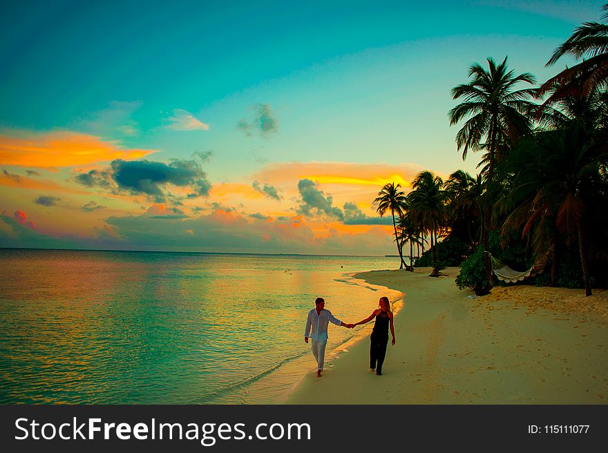 Man And Woman Holding Hand Walking Beside Body Of Water During Sunset