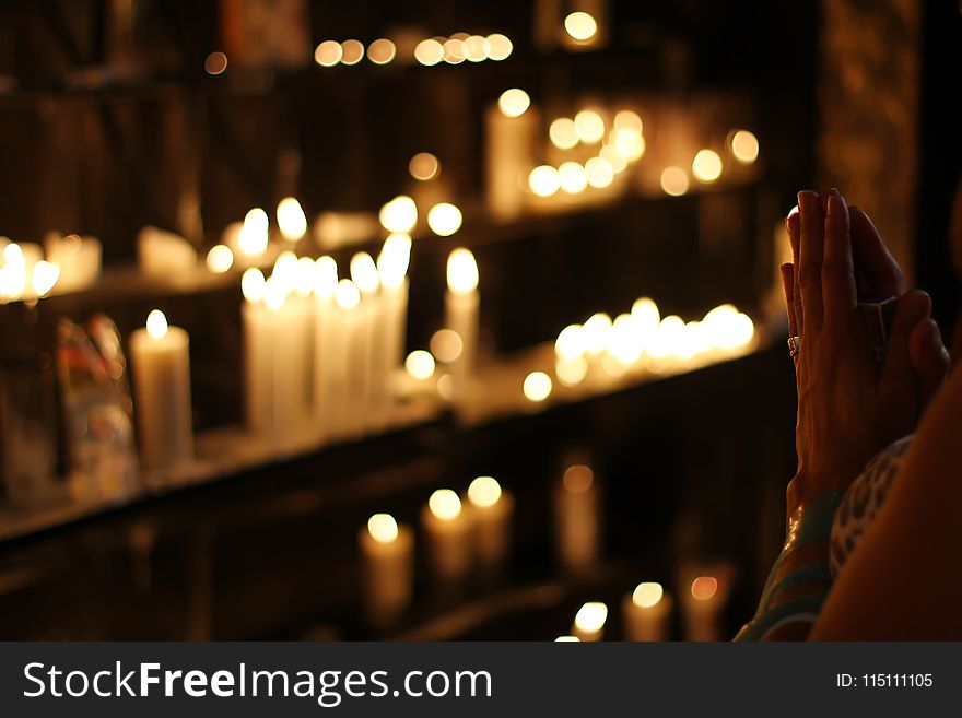 Close Up Photograph of Person Praying in Front Lined Candles