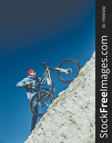 Young guy with a bicycle on a chalky mountain against a blue sky