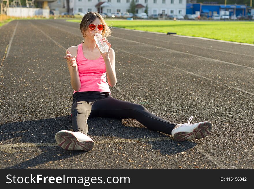 Beautiful teenage girl resting after workout at stadium, girl sat down to relax, drinking water. Beautiful teenage girl resting after workout at stadium, girl sat down to relax, drinking water