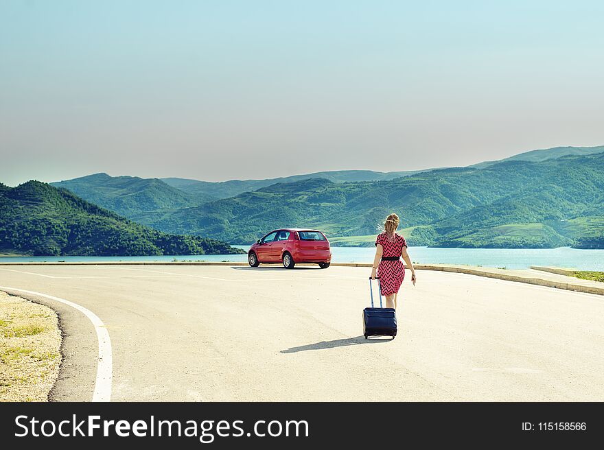 Woman with suitcase at the road with a red car