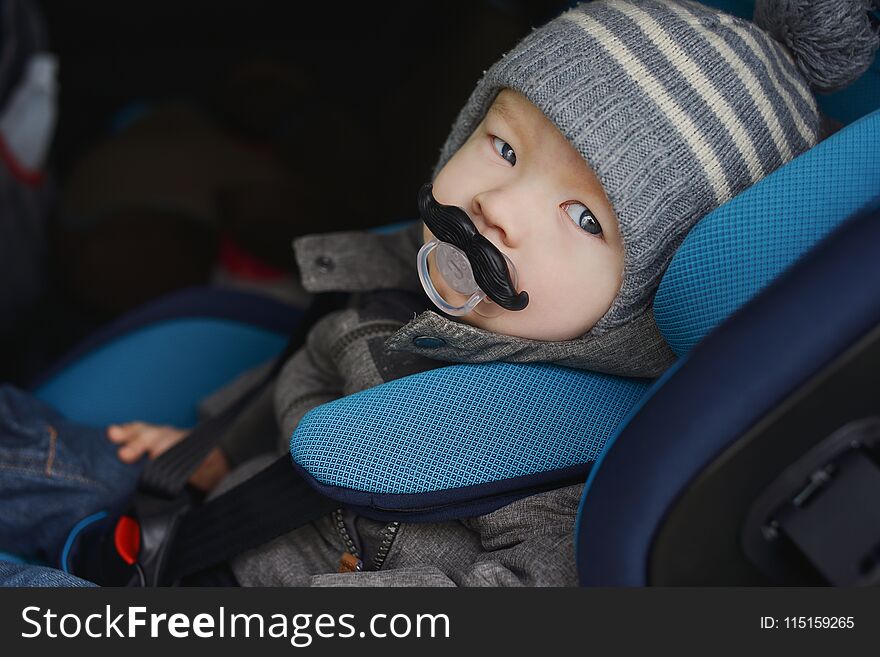 Baby boy in car seat with funny dummy in mouth