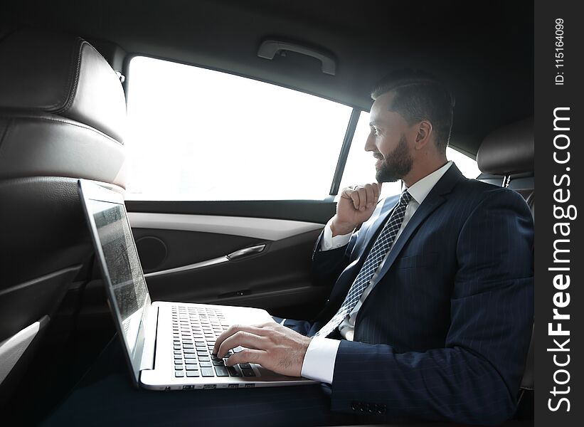 Businessman typing text on laptop sitting in modern car. Businessman typing text on laptop sitting in modern car