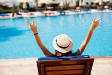 Rear View Of Young Beauty Woman In Straw Hat Relaxing With Hands Up On Chaise-lounge By The Pool Royalty Free Stock Photography