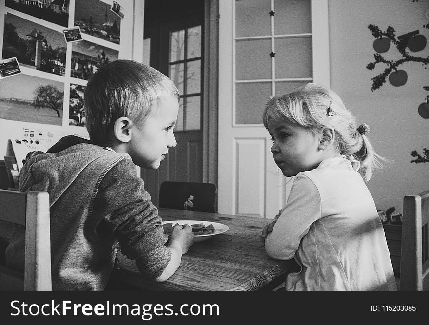 Grayscale Photo of Boy and girl sitting on a dining table chairs