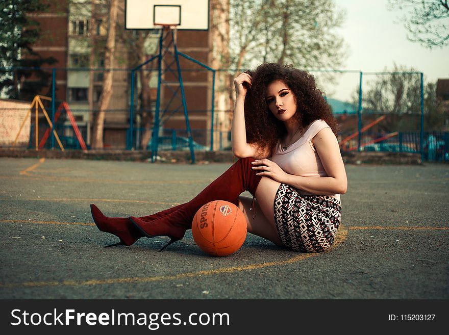 Photo of Woman Sitting on Basketball Court Beside Ball