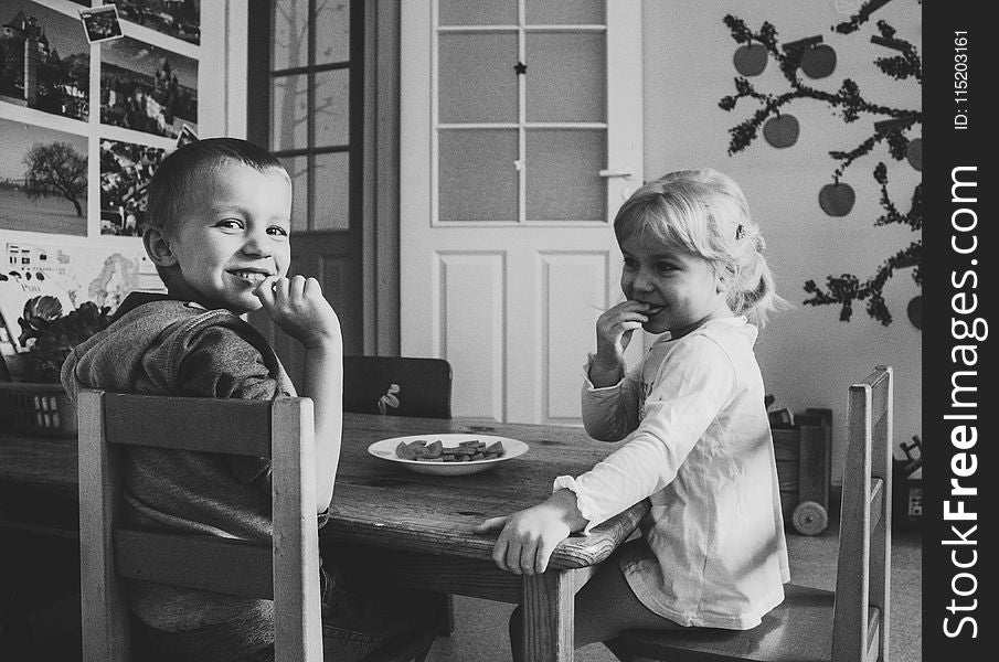 Grayscale Photo of Two Kids Sitting on Dining Table chairs