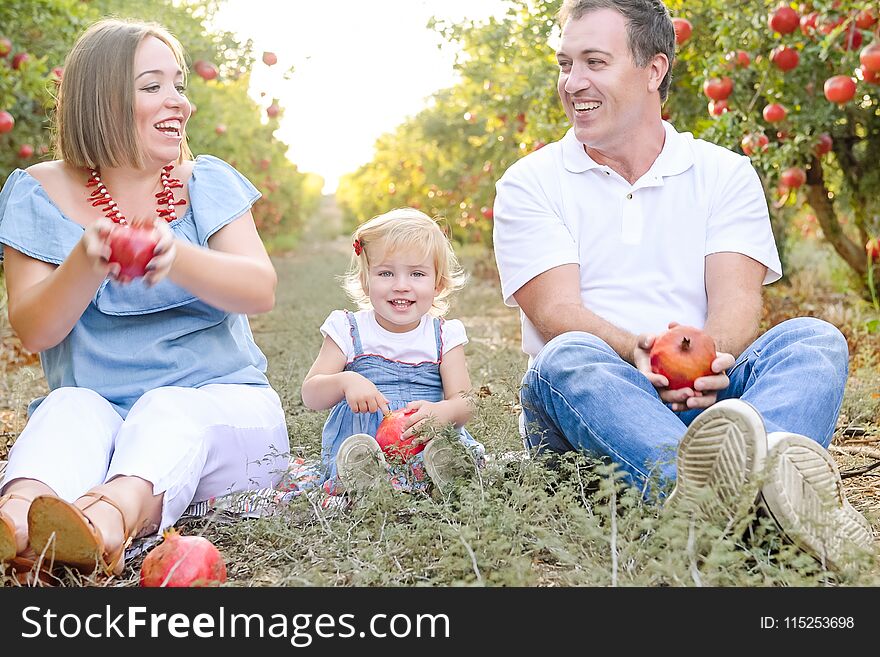 Portrait of happy smiling and laughting parents with cute baby daughter having fun in the pomegrate fruit garden. Harvest, Family vacation concept. Sunset light. soft selective focus, space for text