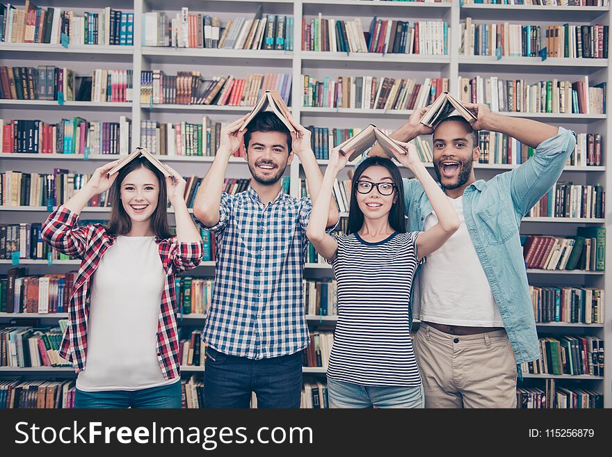 Classmates, international friendship, fun and teenage concept. Group of four cheerful students teenagers in casual outfits with books in the form of a roof over the head fooling around in library