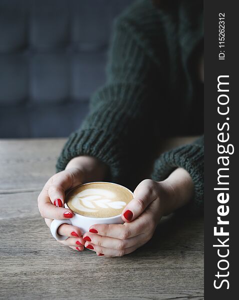 Female hand hold coffee cup with heart shape on wooden table.