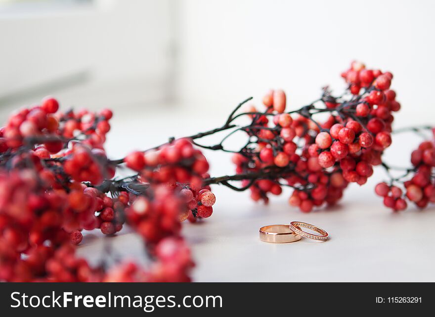 Two gold wedding rings with a diamond near the red berries.