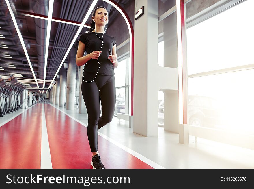 Athletic sporty fit girl with headphones running on run track in gym. Athletic sporty fit girl with headphones running on run track in gym